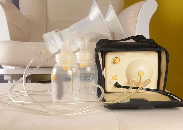 Image of bottles and a breast pump on a table, with a mom and baby in background